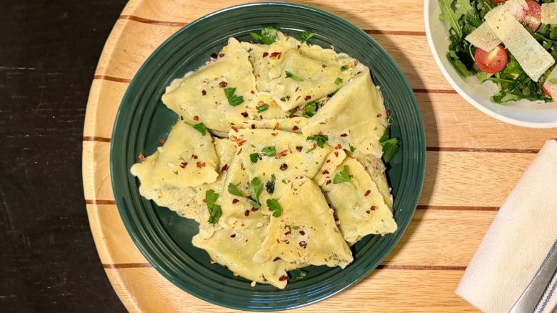 Pasta Prima Spinach & Mozzarella Ravioli on a plate on with basil next to an arugula salad, fork, and knife