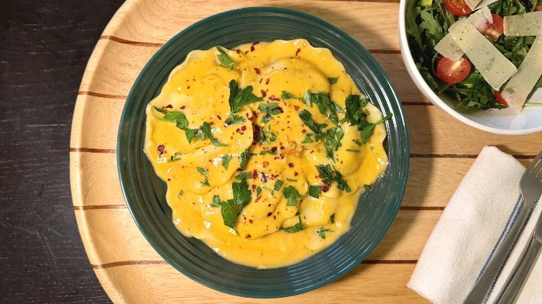 Rana Shrimp Ravioli with Lobster Sauce on a plate on with basil next to an arugula salad, fork, and knife