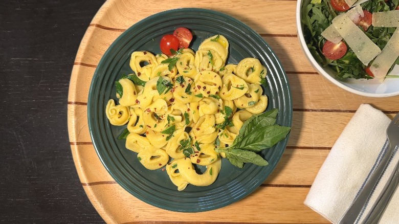 Servioli Five Cheese Tortellini on a plate on with basil next to an arugula salad, fork, and knife
