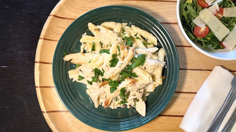 Costco Chicken Alfredo on a plate on with basil next to an arugula salad, fork, and knife