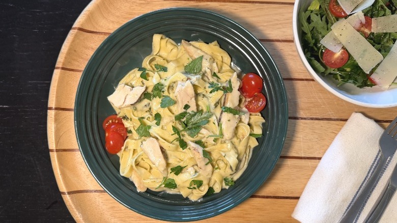 Rana Chicken Alfredo & Spinach Tagliatelle on a plate on with basil next to an arugula salad, fork, and knife