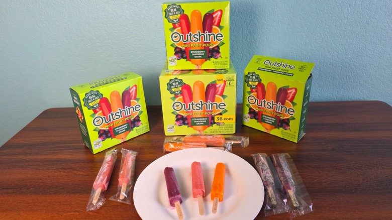 Outshine mini fruit pops boxes, individual packages, and three flavors open on a plate