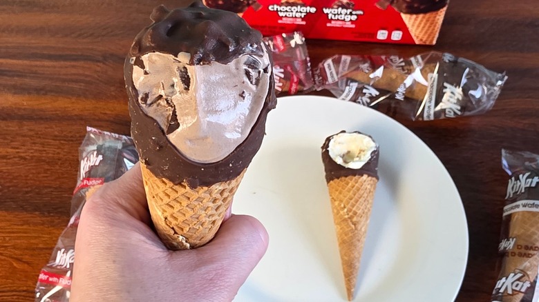 Hand holding KitKat chocolate wafer cone with missing bite and other ice cream in background