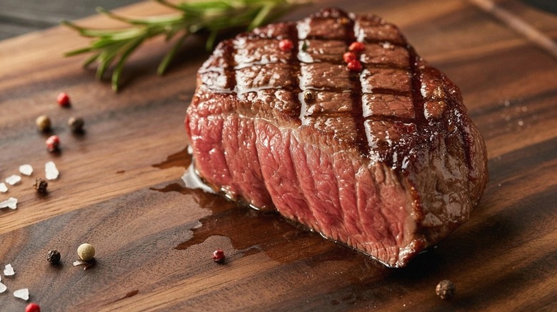 A grilled filet mignon steak with grill marks and garnished with fresh rosemary on a wooden board