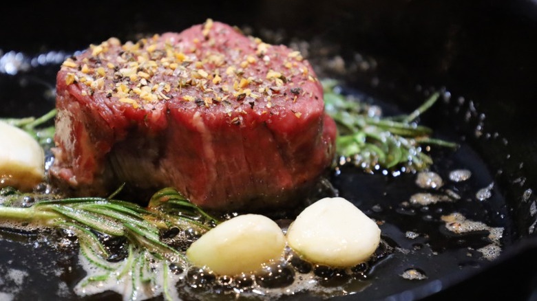 A seasoned filet mignon searing in a pan
