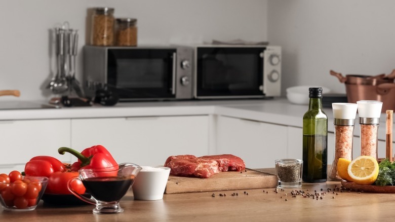 A beef steak on a wooden kitchen top counter surrounded by red pepper and seasoning in a kitchen