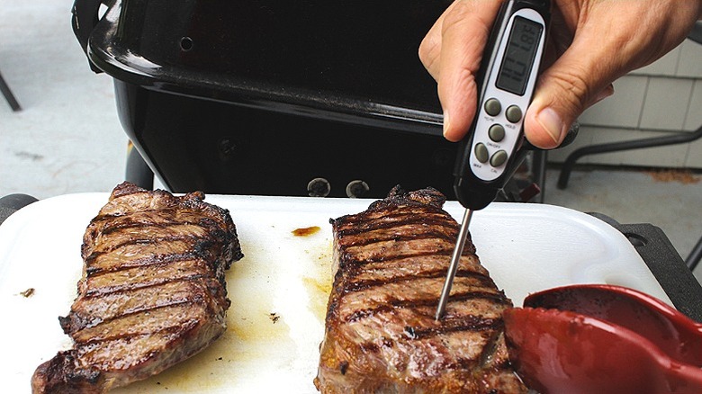 Two pieces of fillet beef off the grill, being checked for temperature