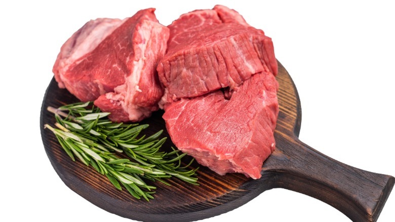 Three pieces of raw filet mignon on a wooden serving board with rosemary sprigs