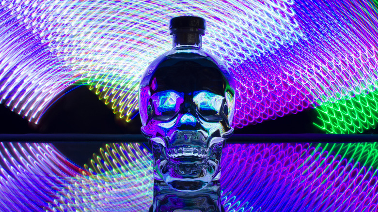 A bottle of Crystal Head Vodka -- a clear skull with a cork on top -- backlit by dazzling purple, blue, and green light