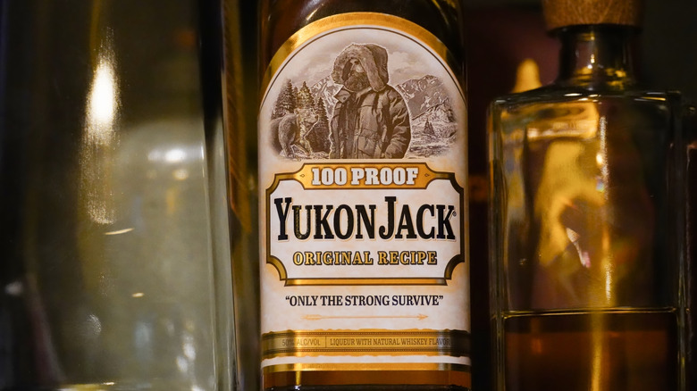 A bottle of 100-proof Yukon Jack, brown glass with a yellow-trimmed white label.