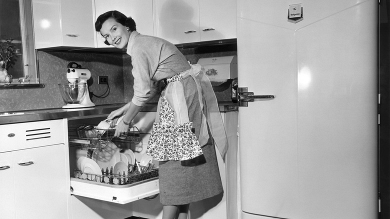 Black and white photo of a woman using an appliance in a vintage 1950s kitchen