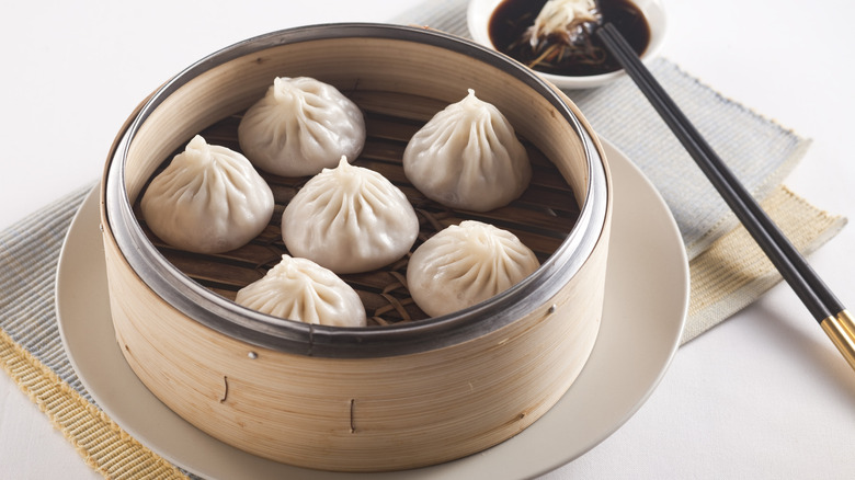 A basket of soup dumplings with sauce on the side