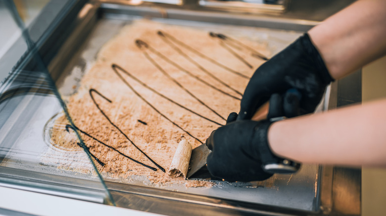hand using a spatula to roll ice cream in a frozen pan
