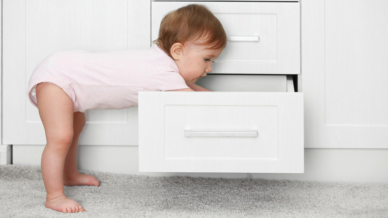toddler leaning over into kitchen drawer