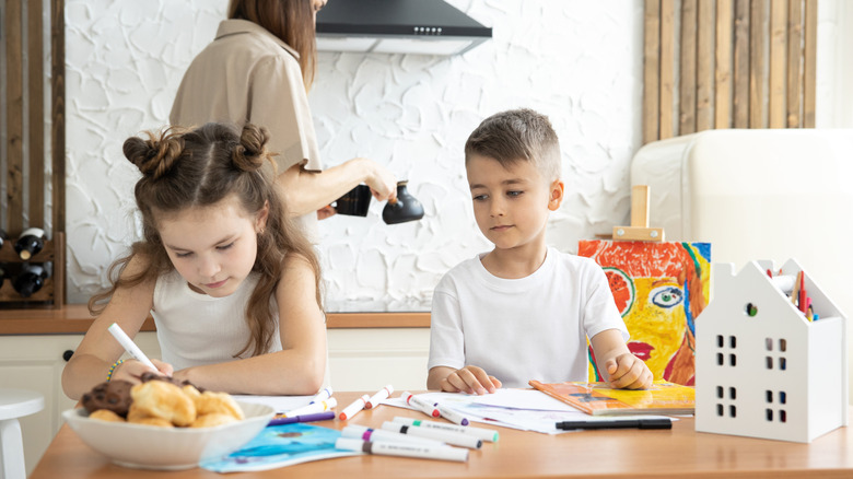 mother cooks while two kids work on art projects in kitchen