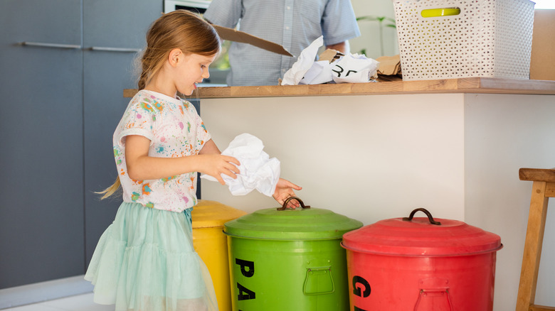 girl puts trash into paper recycling bin in kitchen
