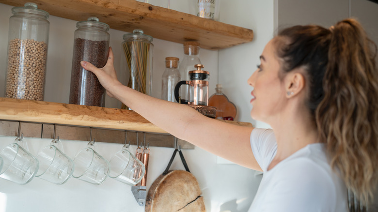 woman reaches for item on kitchen shelf