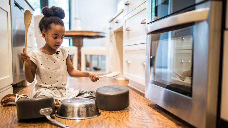 child playing with pots and pans on the kitchen floor