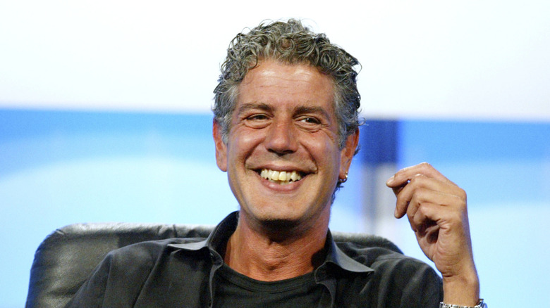 Anthony Bourdain smiling with his closed left hand in the air
