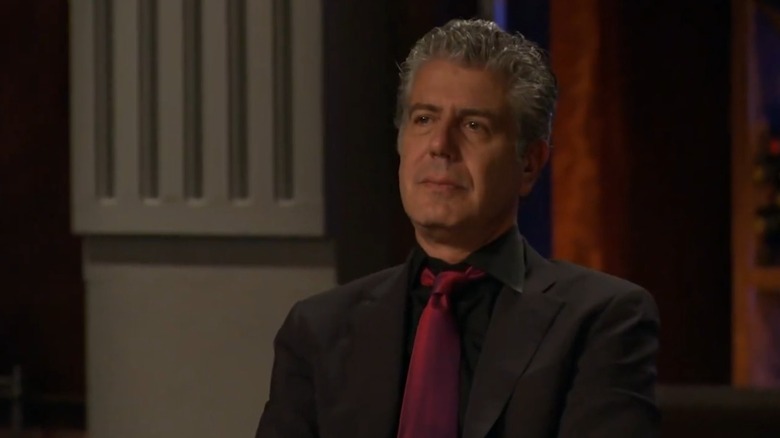 Anthony Bourdain on Top Chef, wearing a black suit and shirt with red tie