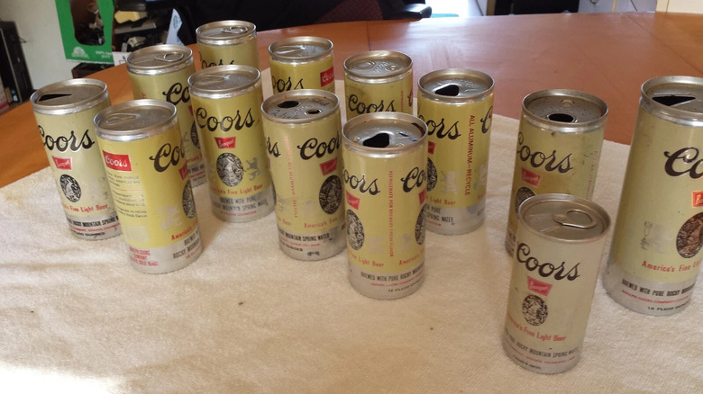 Lot of 13 cans of vintage Coors cans with a mix of popped and unpopped tops on a wooden table