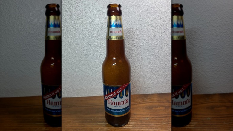A bottle of Hamm's on a wood surface against a white wall