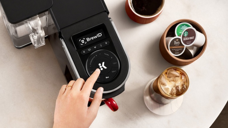 Hand pressing button on top of Keurig coffee machine