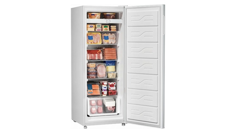 A white upright freezer open and full of frozen goods