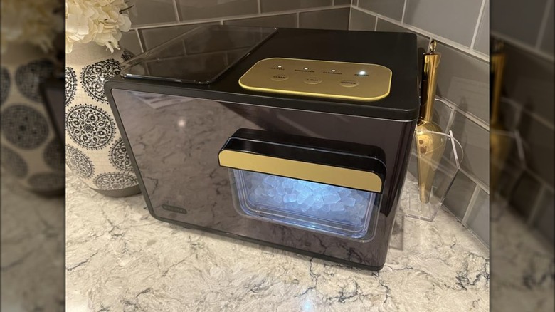 A black rectangular countertop ice maker with gold accents