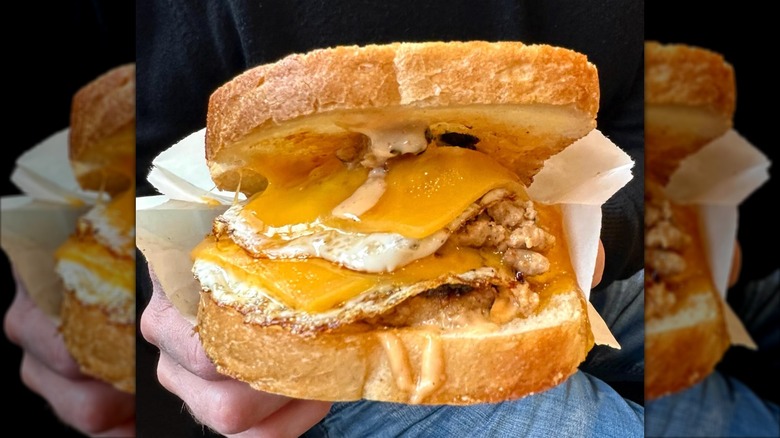 Person holding a Yolko Ono fried egg sandwich with two sausage patties and cheese