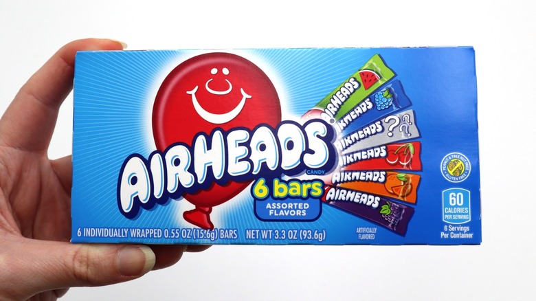 A hand holding a box of Airheads on a white background
