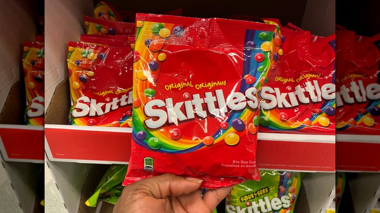 A hand holding a bag of Skittles in a store