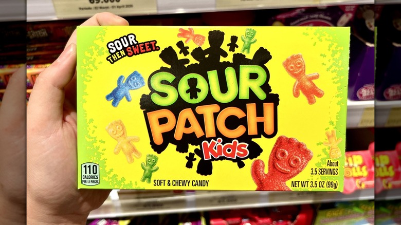 A hand holding a box of Sour Patch Kids in a store
