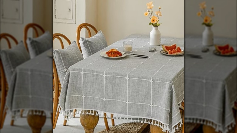 A gray tablecloth on a kitchen table with plates of cut up fruit and flowers on top