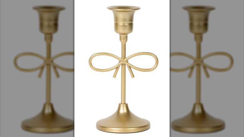 A golden candle holder with a bow in the center made of the piece itself