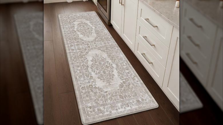 An off-white kitchen mat with a Persian design on a wooden floor next to white cabinet