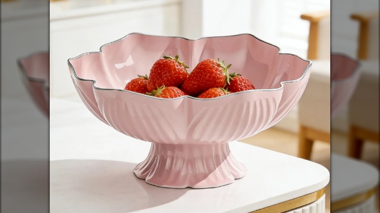 A pink bowl on a white table with strawberries in it