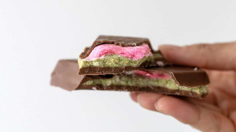Hand holding milk chocolate bar with pistachio and pink filling