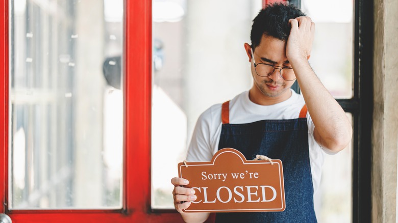 A disappointed breakfast chain owner holding a closed sign
