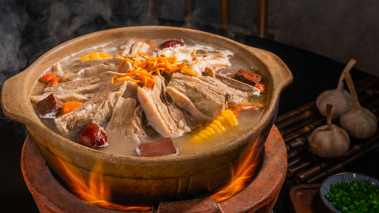A pot of Chinese-style soup cooking on a live fire with alliums in the background