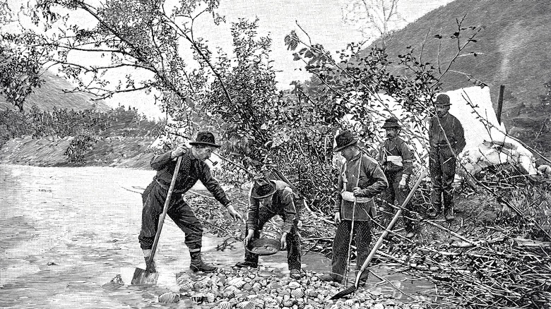 A vintage black-and-white illustration of men panning for gold along the rocky shores of a California river