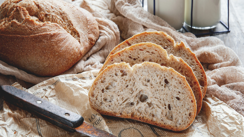 Whole and sliced sourdough with a rusty bread knife on a rustic background