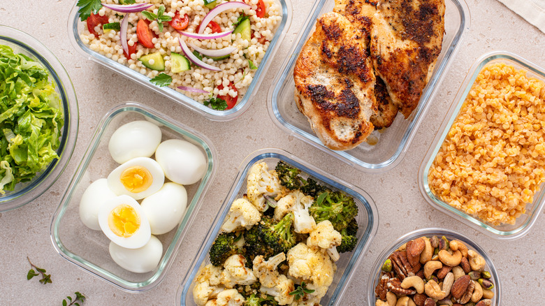 Glass containers filled with prepared foods, like couscous, roast chicken, hard-boiled eggs, steamed broccoli and cauliflower, and rice