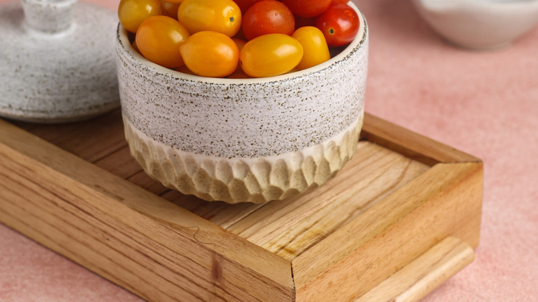 A bowl of tomatoes sit on a wooden kitchen riser