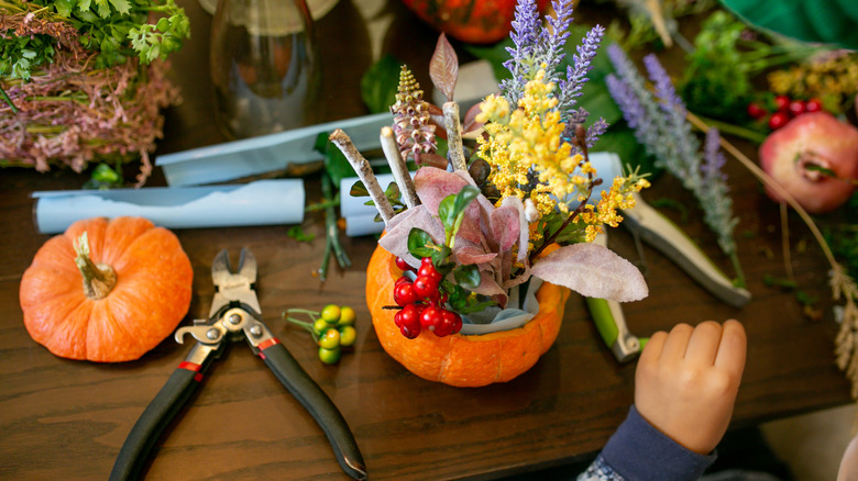 A person constructs a Thanksgiving centerpiece out of a pumpkin and dried and artificial plants