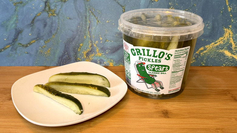 Pickle spears on a plate, next to large container of pickles