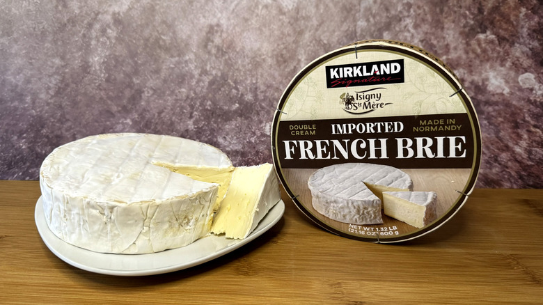 A wheel of brie on plate next to its packaging