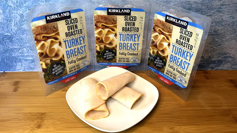 A three-pack of sliced turkey breast in front of plate of turkey