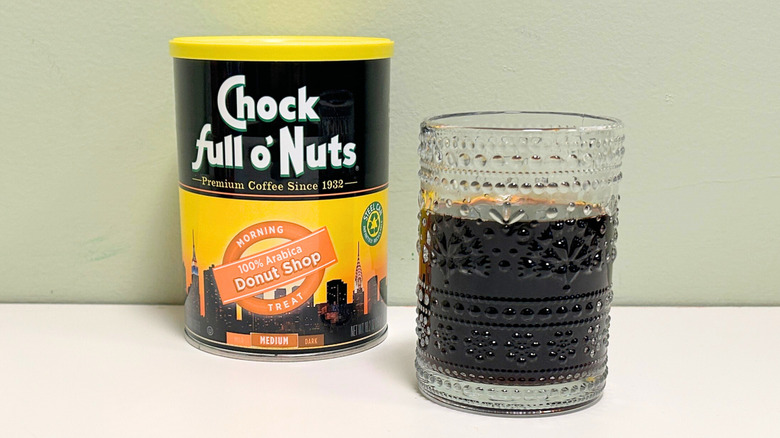A glass cup filled with coffee next to a can of Chock Full O Nuts Donut Shop Coffee