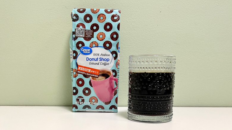 A glass cup filled with coffee next to a bag of Great Value Donut Shop Ground Coffee